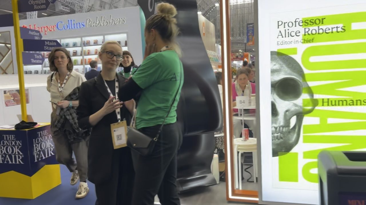 Visitors at the HarperCollins stand, beside a large display for Professor Alice Roberts