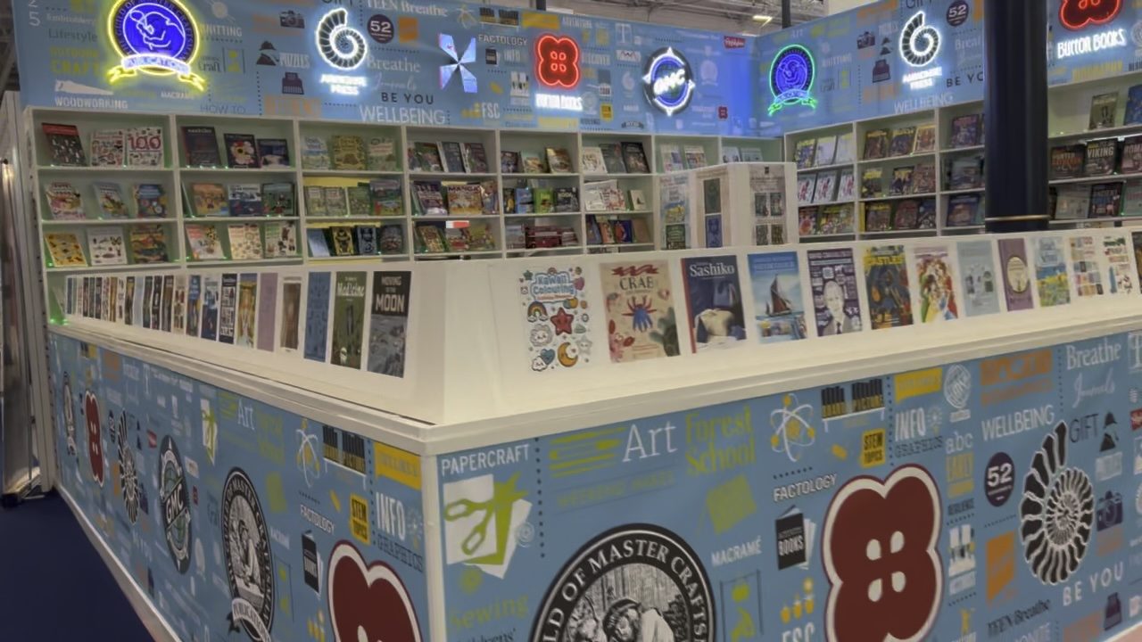 A specialist illustrated-book stand at the London Book Fair, with shelves of craft titles and neon category signs